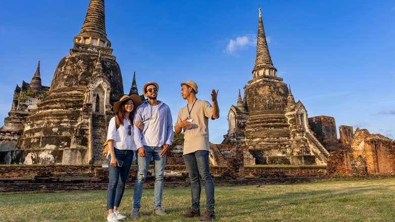 A couple talks with a guide near Southeast Asian stupas