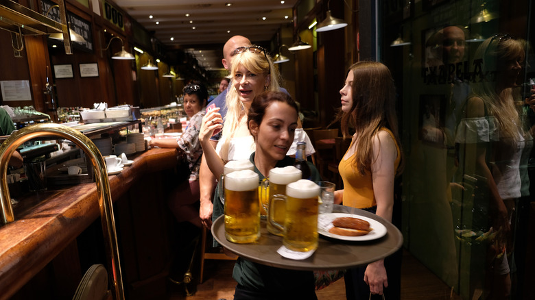 A bartender carries three tankards of beer in a bar in Spain