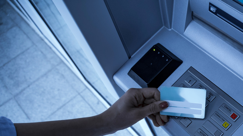 Camera view of hand holding a credit card at an ATM.