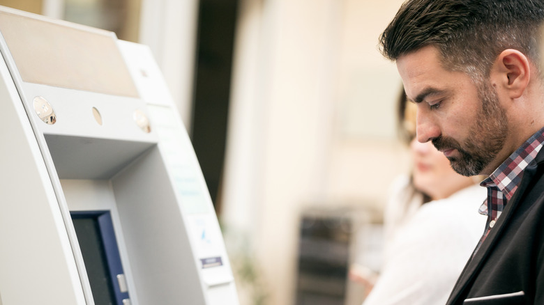 A woman eyes a man as he enters his PIN code at an ATM.