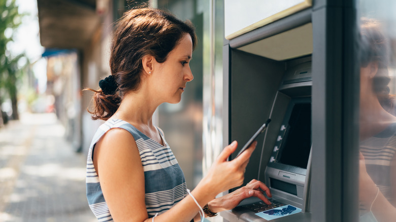 A woman copies her PIN code from her phone at an ATM.