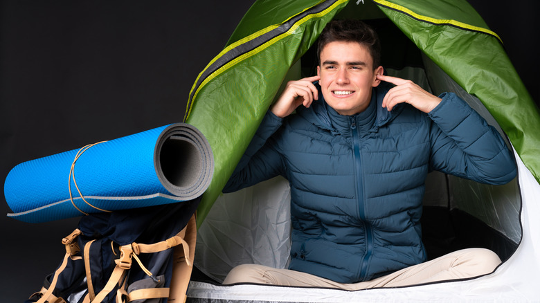 Man plugging ears inside tent 