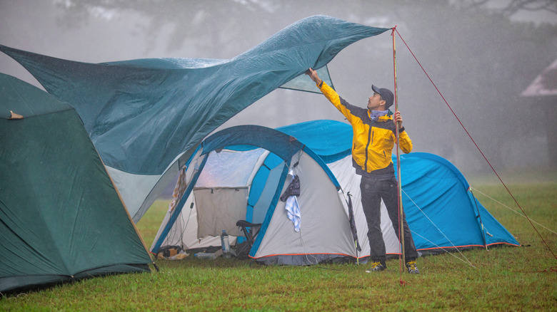 man holding tarpaulin over tent