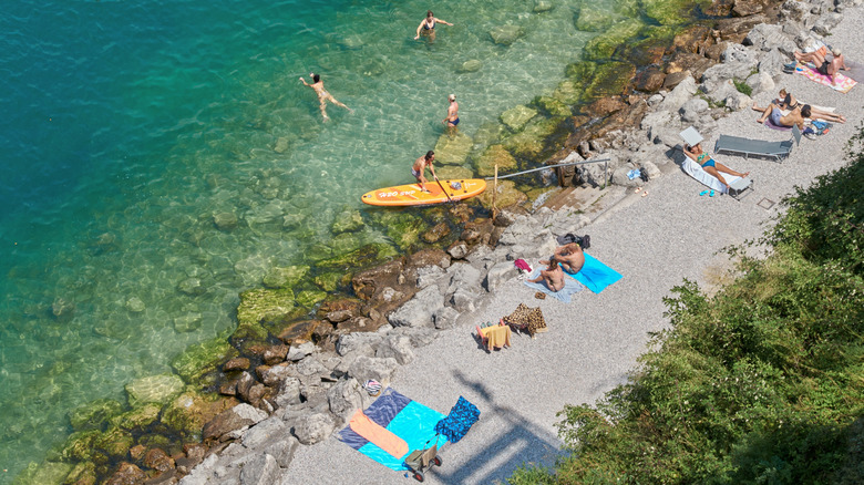 Paddleboarders and loungers on a pebble beach on Lake Garda