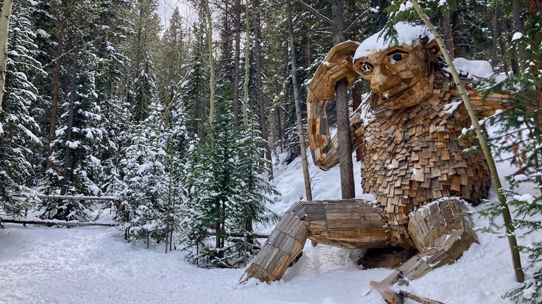 A wooden sculpture of a troll sits along a snowy trail