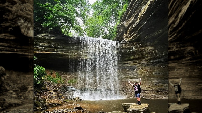 Man posing in front of a tall waterfall