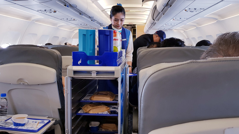 A flight attendant and beverage cart