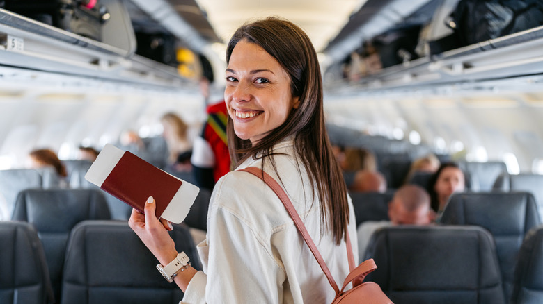 Woman stands in the middle of airplane excited about her travels