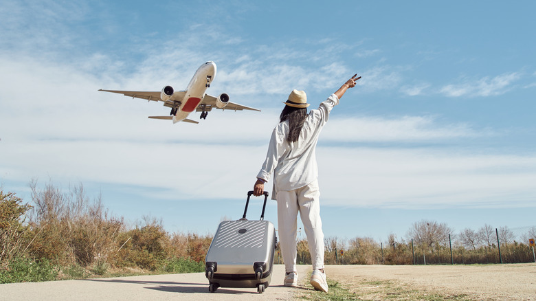 Woman with suitcase watches airplane