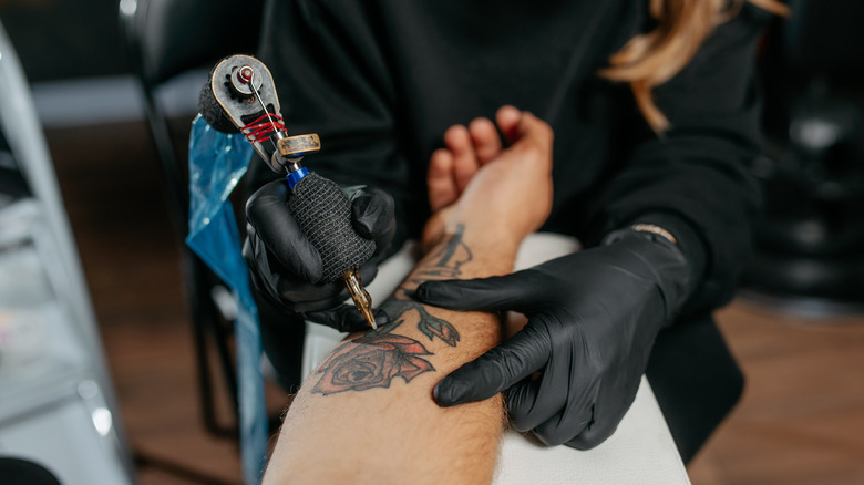 Artist tattooing rose inner arm