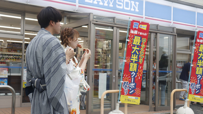 a Japanese couple eating snacks outside of a convenience store