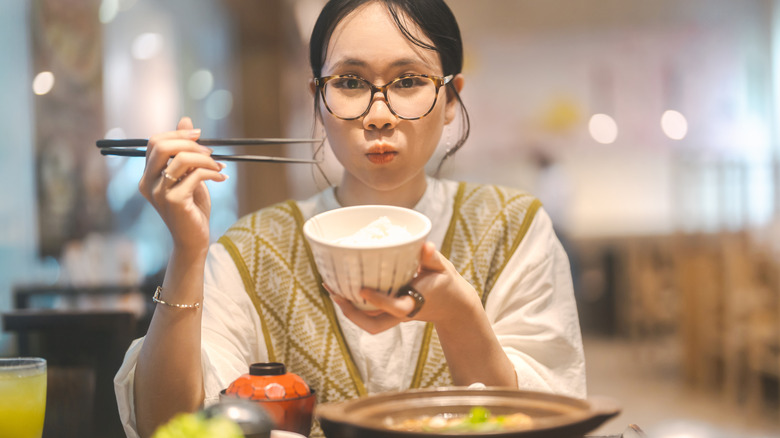 a woman holding a bowl of rice while eating