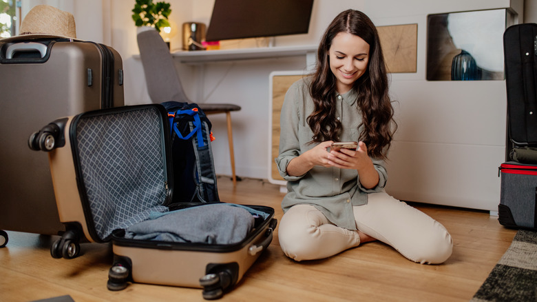 woman packing a suitcase and checking phone