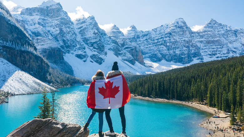 Couple draped in Canadian flag overlooking mountain lake