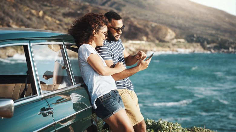 Couple looking at phone next to car