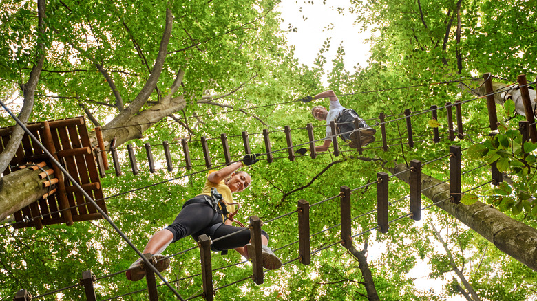 two kids play on a ropes course up high in the trees