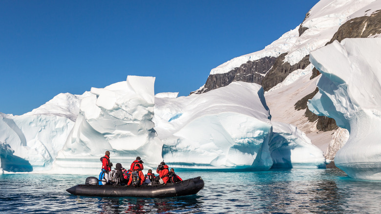 People on inflatable boat in front of  glacier