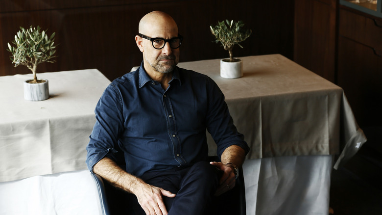 Stanley Tucci posing in front of linen-covered tables.