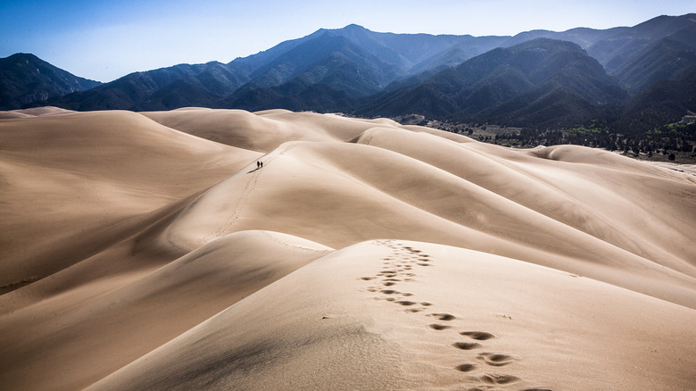 Hikers on sand dunes in Colorado backed by mountains