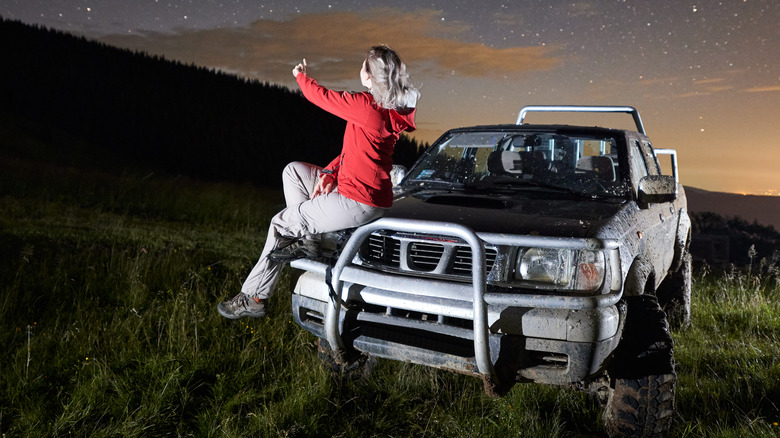 woman stargazing from the hood of a car