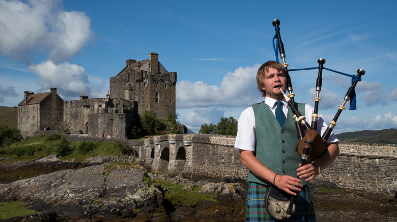 A bagpiper poses in front of Eilean Donan castle.