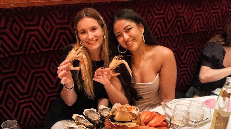 Two women holding up shellfish at Le Dôme Café