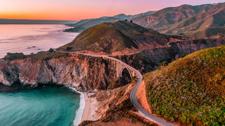 Road over hills by ocean at sunset