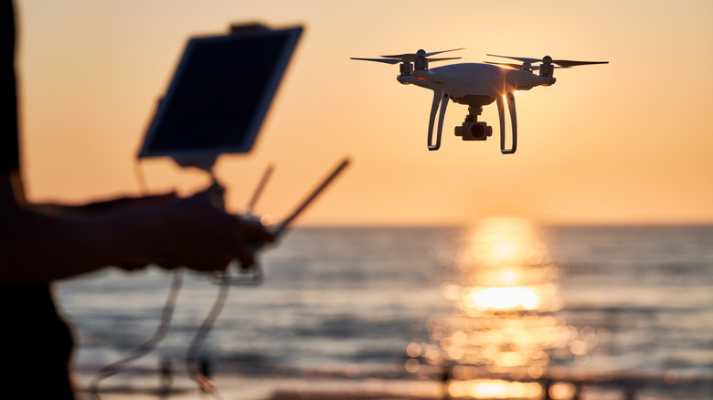 A pilot operates a drone near a sea at sunset