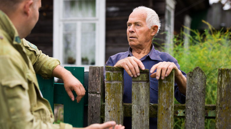 nieghbors chatting on either side of a fence