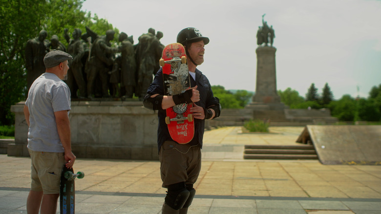 Rainn Wilson holding skateboard in skate park