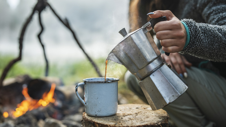 Camper pouring coffee by fire