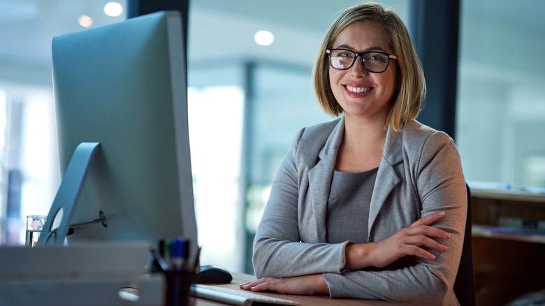 A bespectacled woman smiles near her computer