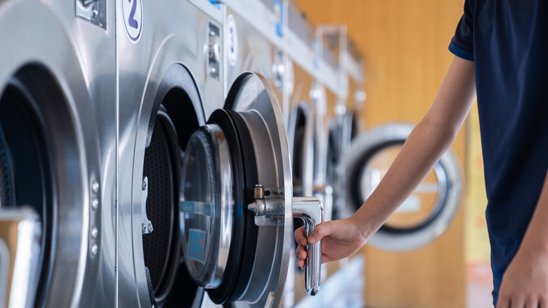 A person opens a washing machine at a laundromat.