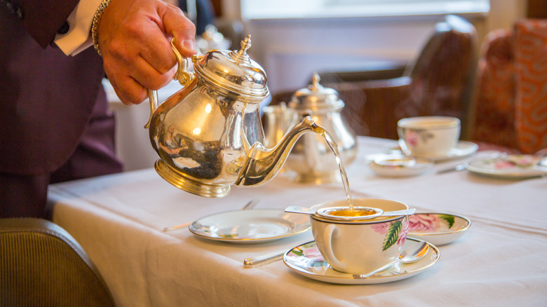 Person pouring silver tea pot