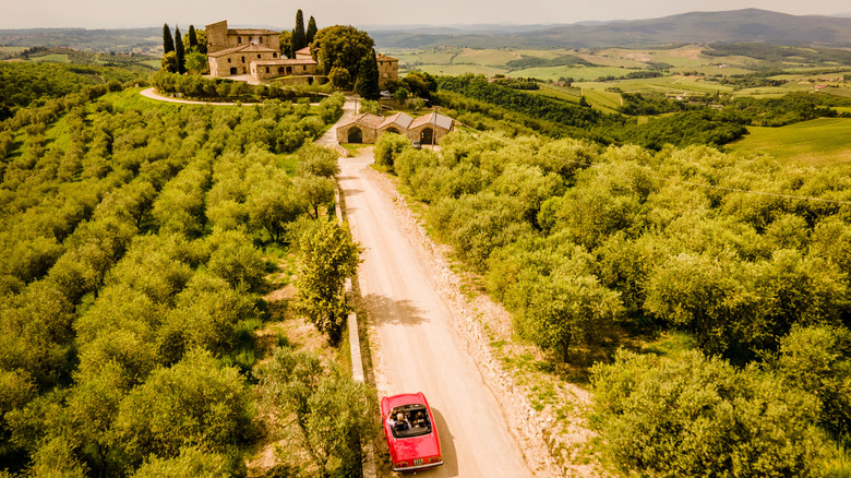 A red car in Tuscany surrounded by greenery.