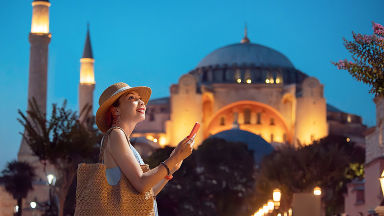 An excited woman holds her phone in front of Hagia Sophia