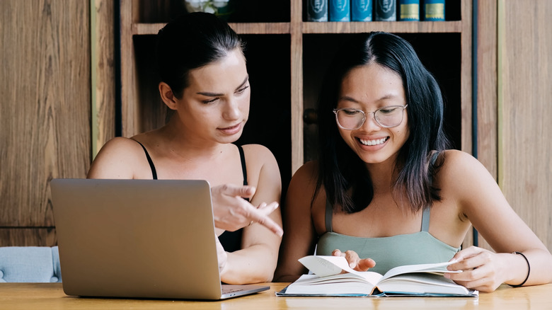 Two women pore over a computer and book