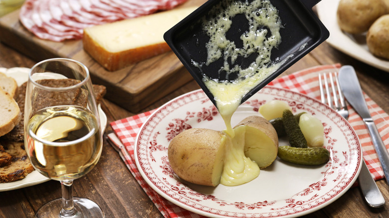 Swiss raclette poured onto a potato on red plate and wooden table