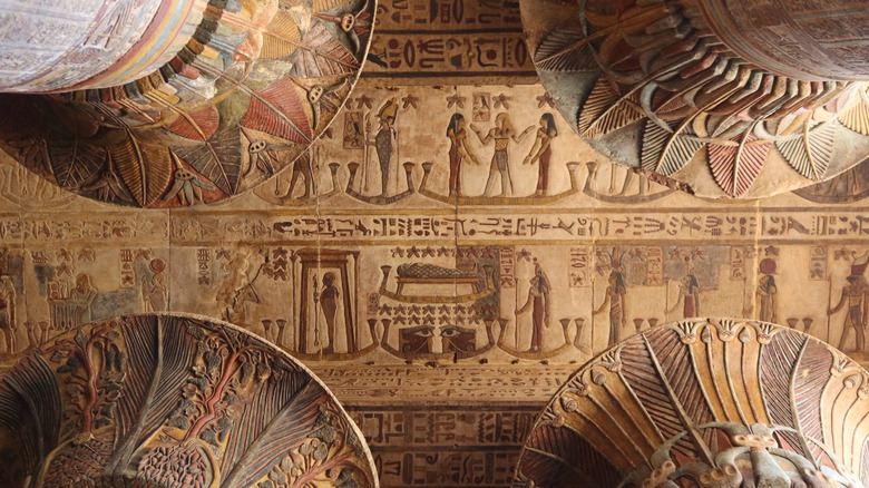 Painted ceiling of the Temple of Esna, showing colorful feather motifs, ancient hieroglyphics, and figures.