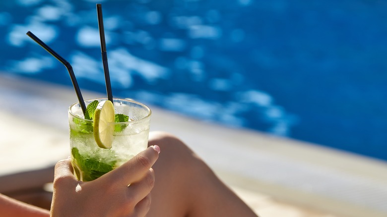 Person holding drink near pool