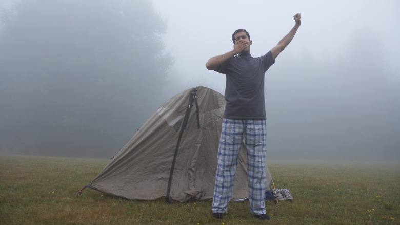 Camper waking up outside tent in pajamas