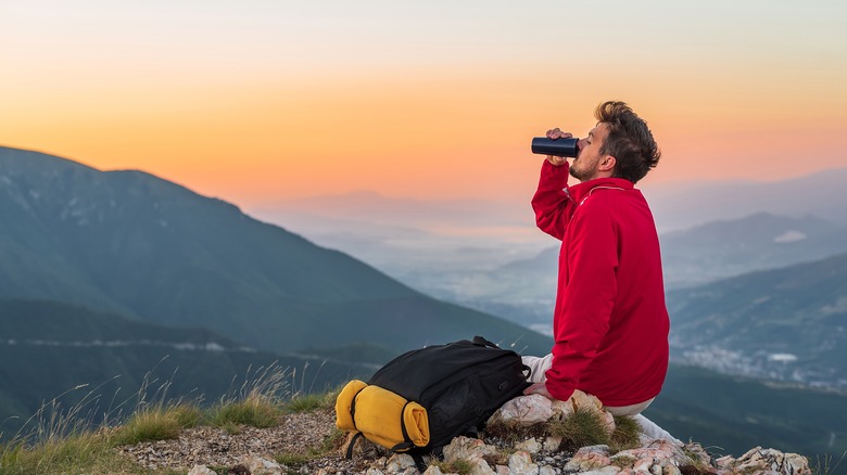 Backpacker drinking water with sunset behind him