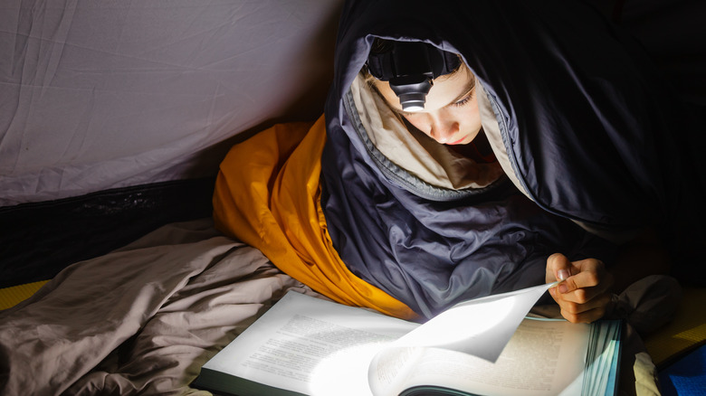 Person reading at night in tent with flashlight