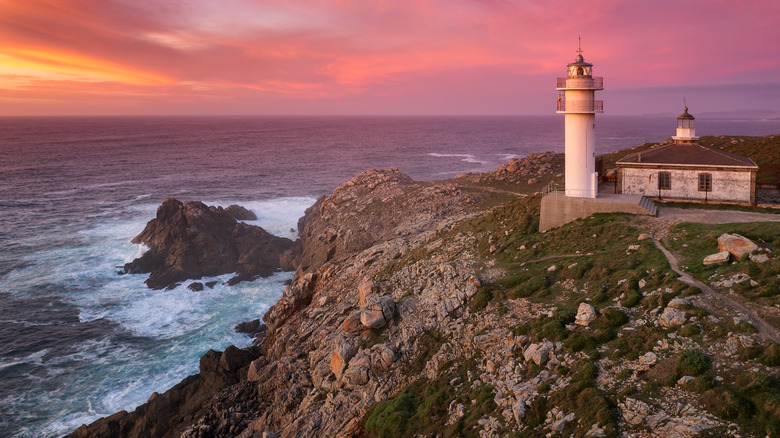 Lighthouse on rocky cliffs overlooking ocean at dusk in Galicia Spain