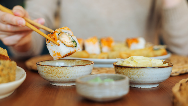 person holding sushi with chopsticks