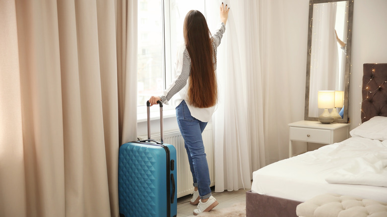 woman with luggage looking out of hotel window