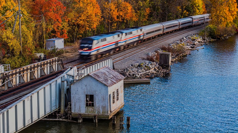 An Amtrak train chugs past a lake and autumnal forest