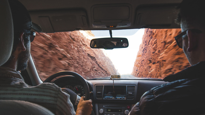 Two men driving in a car past red rock mountains