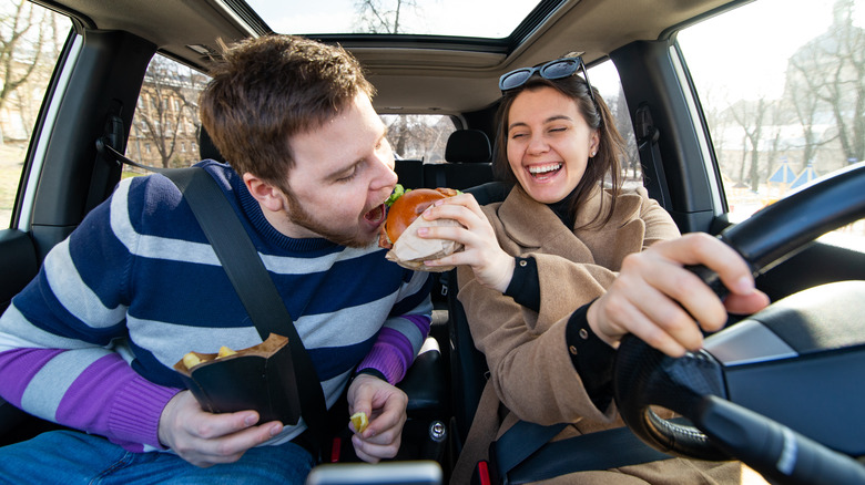 car driver feeding passenger cheeseburger