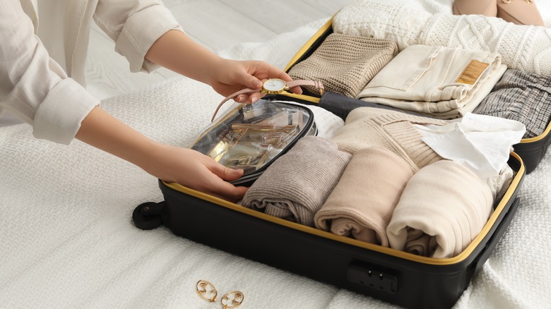 Traveler packing jewelry into suitcase